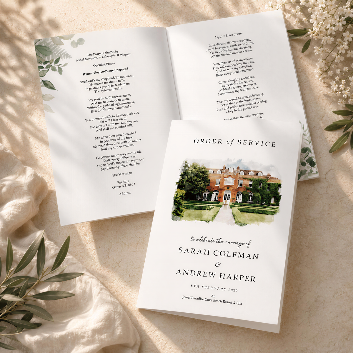 a wedding invitation card with a house illustration and text, placed on a table with greenery.