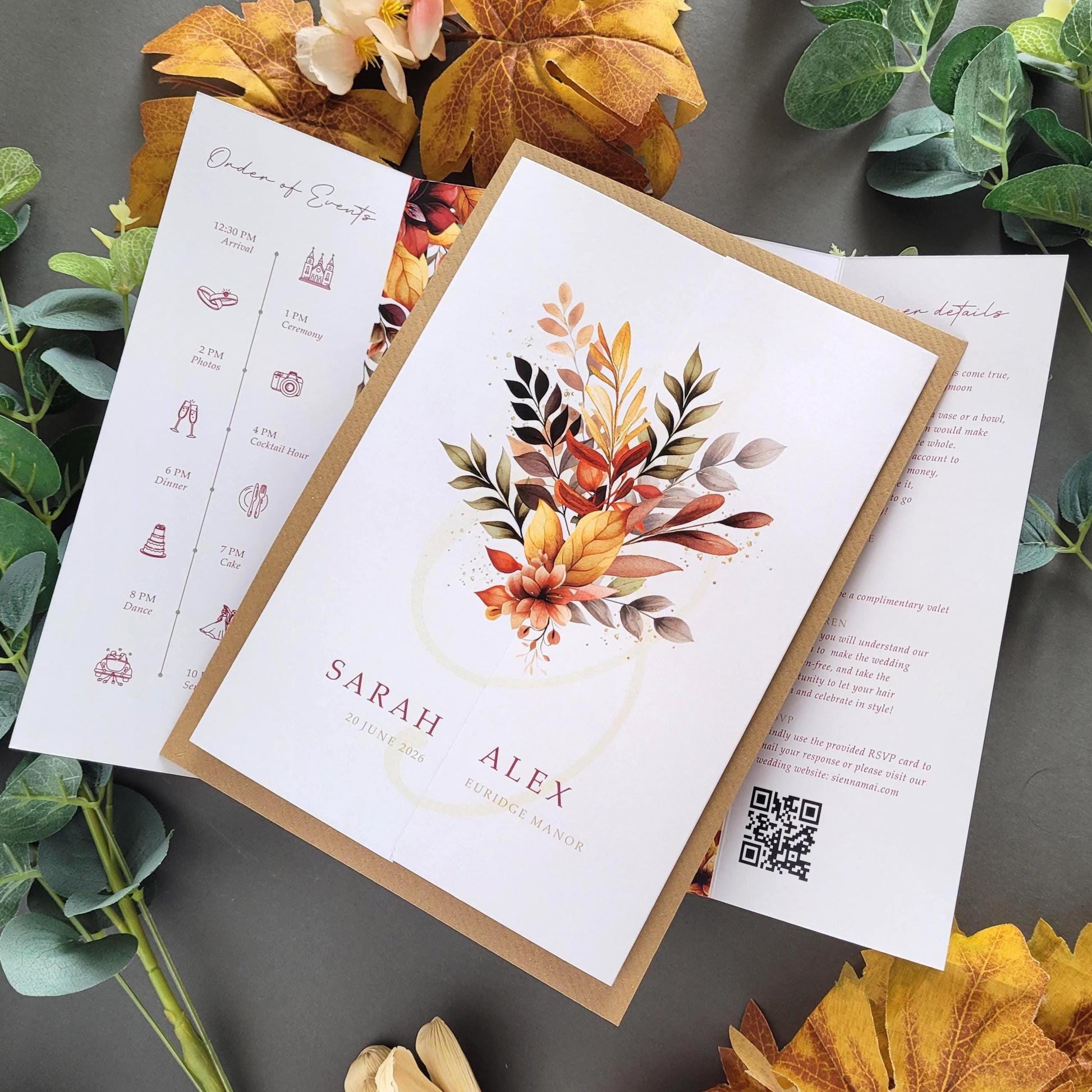a wedding invitation card with a floral design, surrounded by autumn leaves and greenery.