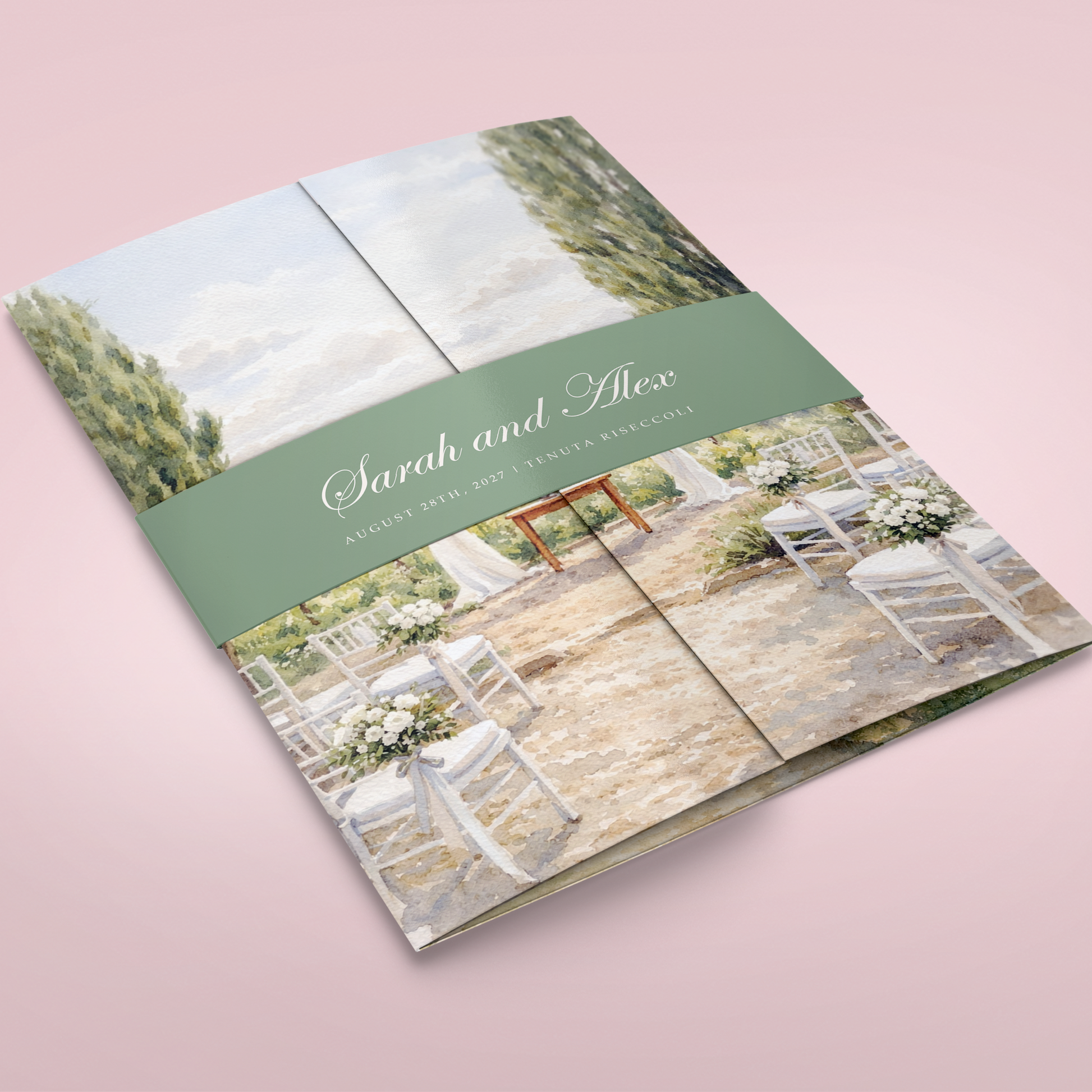 A folded wedding program or brochure with a watercolor-style printed design, shown on a soft pink background. The cover features a sage green band with the names 'Sarah and Alex' in white script, and the rest of the design depicts an outdoor wedding aisle with white chairs, green trees, and a stone floor.