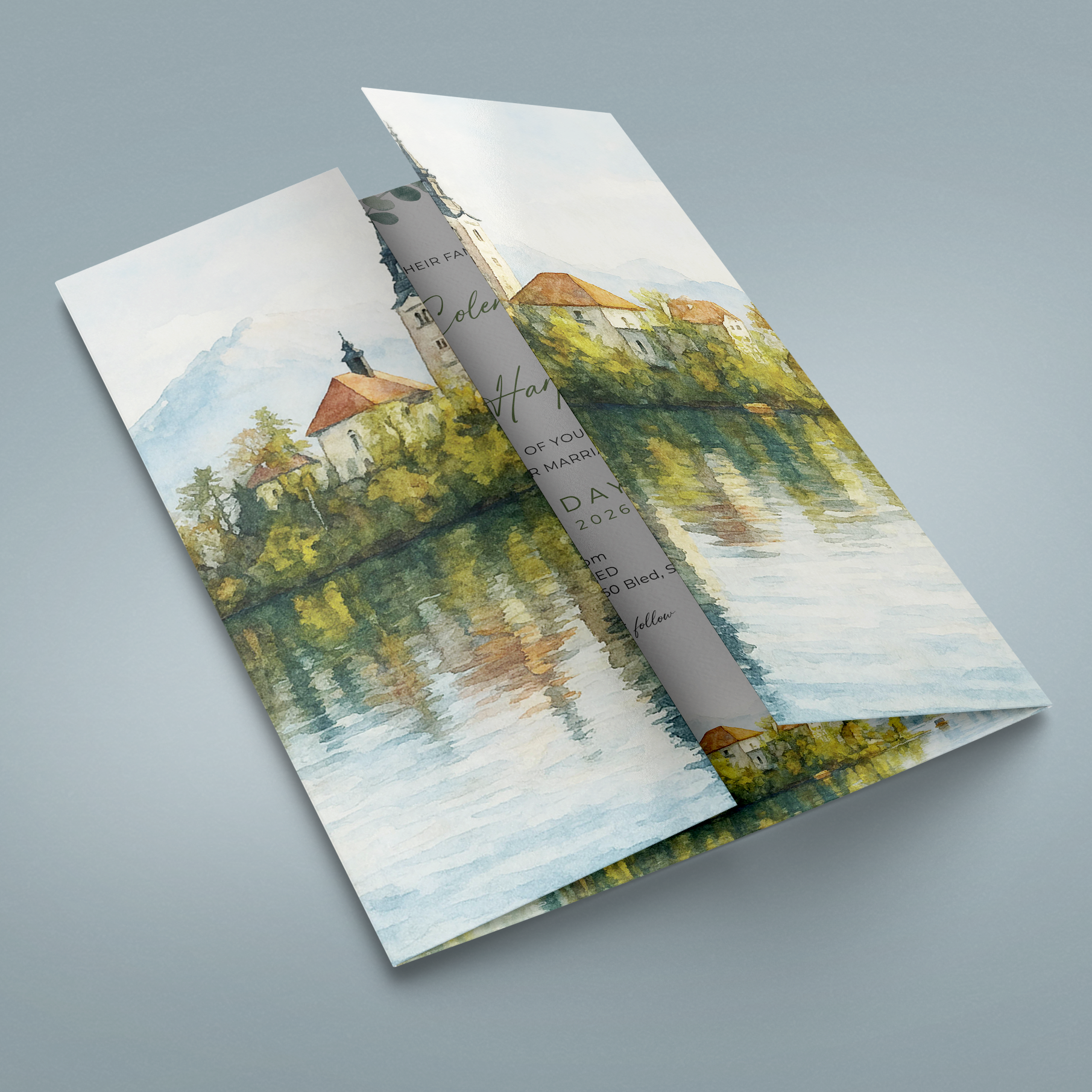 A folded brochure or booklet with a watercolor landscape print of a lakeside village, shown on a smooth light gray background.
