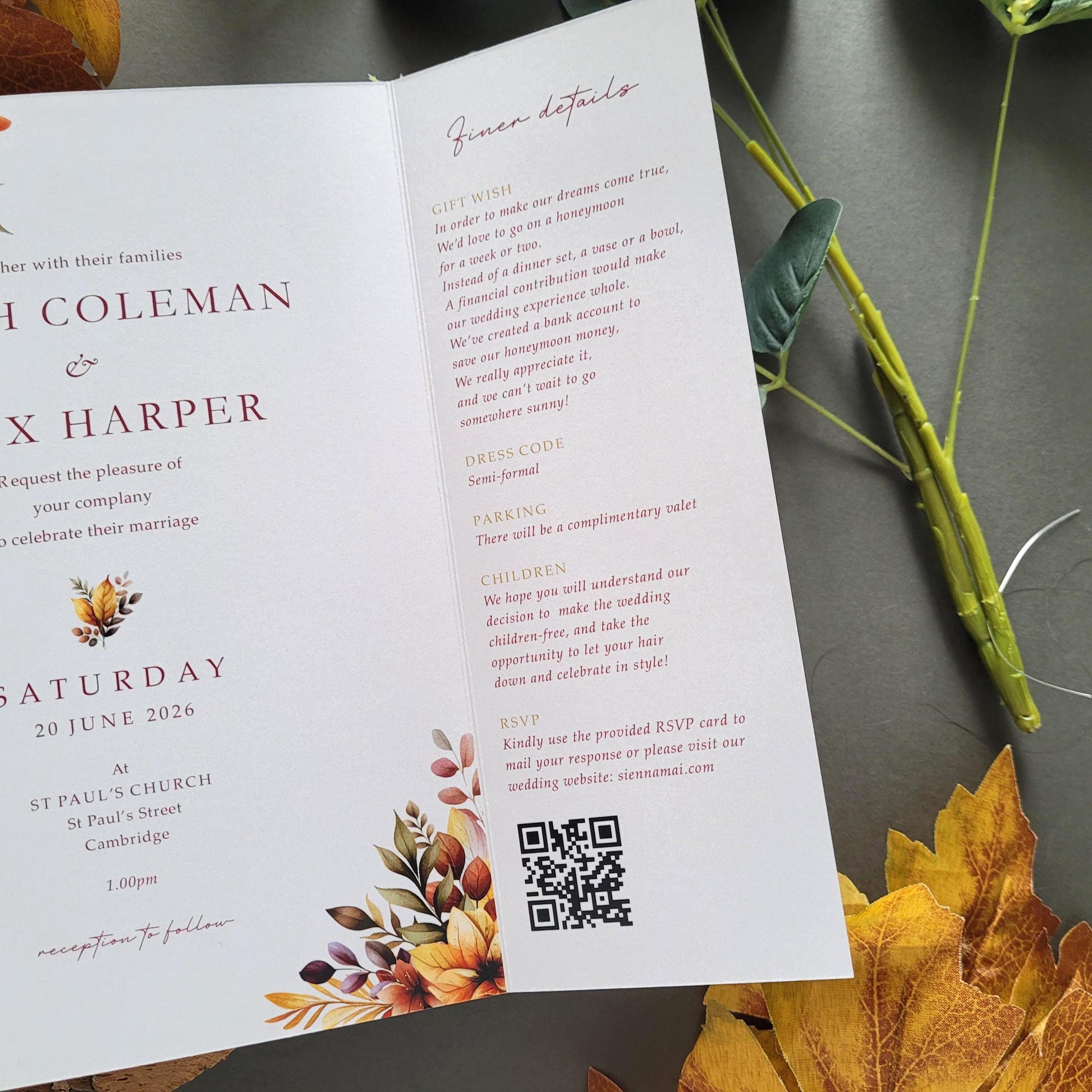 a wedding invitation card with autumn leaves and flowers, placed on a table with a plant and some leaves.